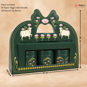 A dark green wooden tea gift box with decorative pink lotus and white cow motifs, shown with dimension lines indicating 32 cm width, 26 cm height, and 8 cm depth. The box contains three round tin boxes and is photographed on a beige background with text noting included paper bags and round tin boxes.