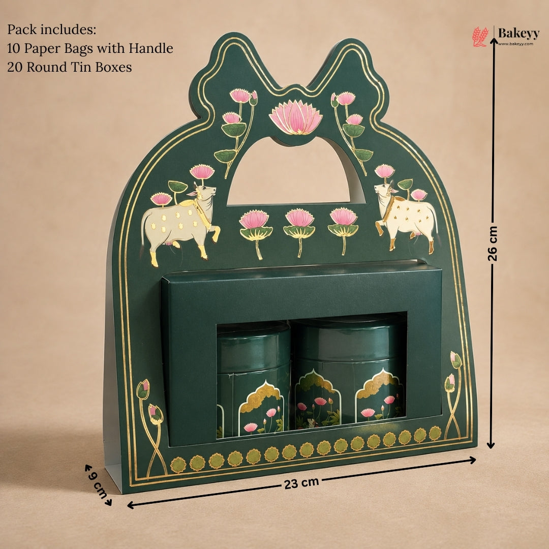 A dark green decorative gift box with gold detailing, pink lotus flowers, and cow illustrations, shown with dimension markers indicating 26 cm height, 23 cm width, and 8 cm depth. Two matching green cylindrical tins are placed inside a front slot.