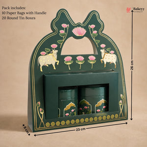 A dark green decorative gift box with gold detailing, pink lotus flowers, and cow illustrations, shown with dimension markers indicating 26 cm height, 23 cm width, and 8 cm depth. Two matching green cylindrical tins are placed inside a front slot.