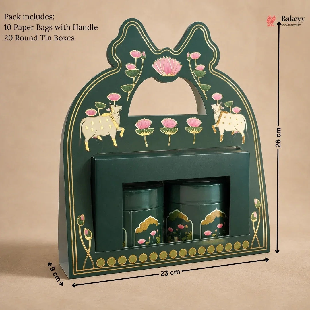 A dark green decorative gift box with gold detailing, pink lotus flowers, and cow illustrations, shown with dimension markers indicating 26 cm height, 23 cm width, and 8 cm depth. Two matching green cylindrical tins are placed inside a front slot.