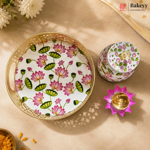 A decorative round tray and matching small container set with a pink and green lotus flower pattern on a white background, styled on a beige surface with a gold-toned flower-shaped candle holder and floral props.