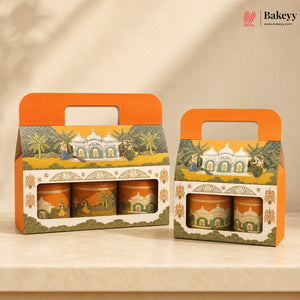 Two orange and cream gift boxes containing three decorated tea or spice tins, displayed on a beige surface against a warm beige background. The packaging features traditional Indian-style illustrations of domed buildings, palm trees, and figures.