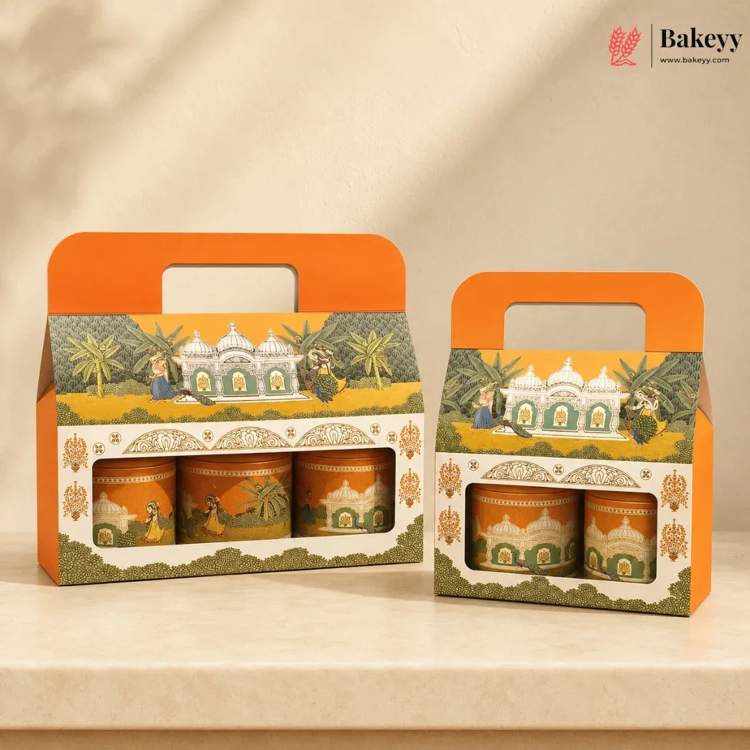 Two orange and cream gift boxes containing three decorated tea or spice tins, displayed on a beige surface against a warm beige background. The packaging features traditional Indian-style illustrations of domed buildings, palm trees, and figures.