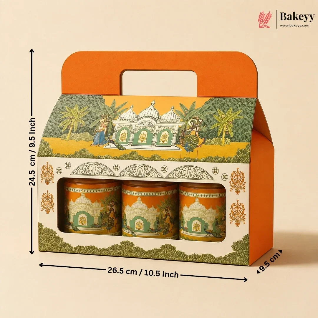 A boxed set of three decorative cylindrical containers with a hinged orange handle lid, shown on a beige background with printed dimensions around it. The packaging features an illustrated architectural scene with green, yellow, and orange tones.