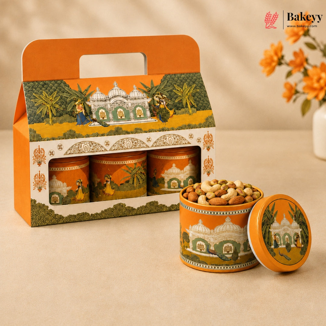 An orange and green illustrated gift box containing three cylindrical tin jars, with one open tin and its lid placed in front, filled with nuts. The packaging features a warm architectural scene with domes and palm trees.