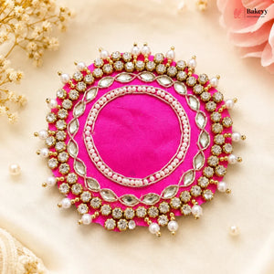 Decorative pink circular piece with gold and pearl embellishments on a beige background.