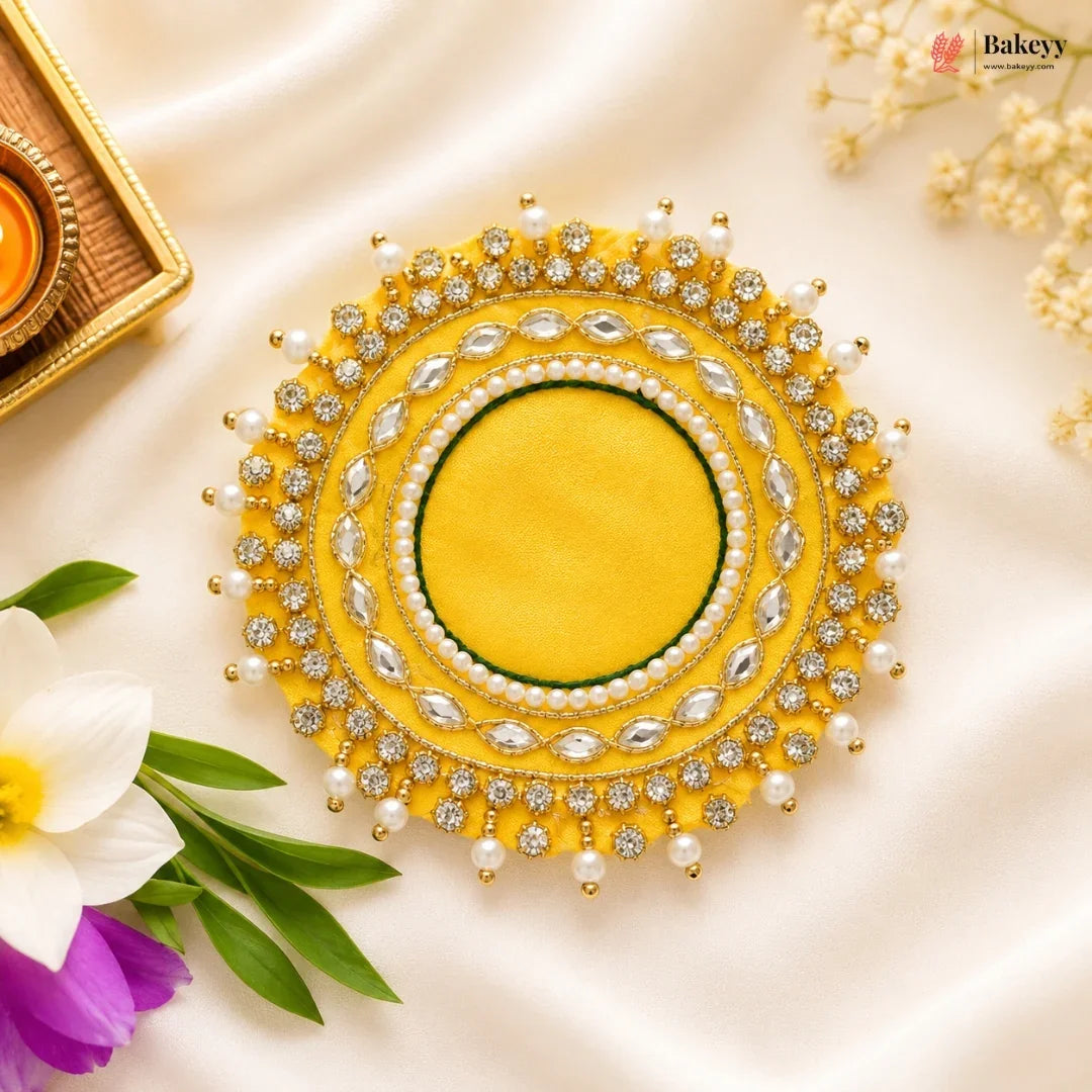 Decorative yellow circular piece with pearls and crystals on a light background with flowers and a decorative box.