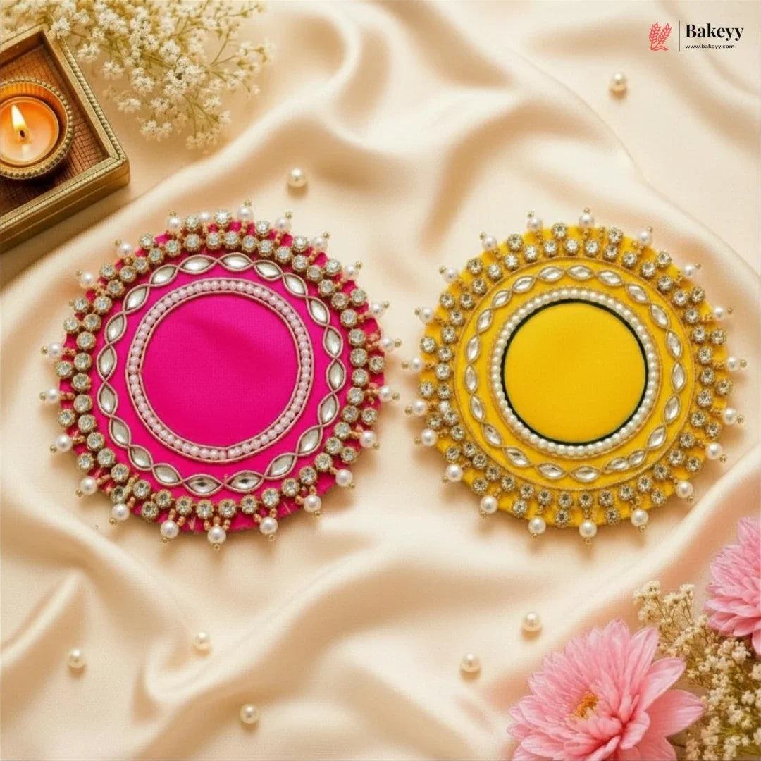 Two decorative plates, one pink and one yellow, on a textured beige surface with flowers and a candle.