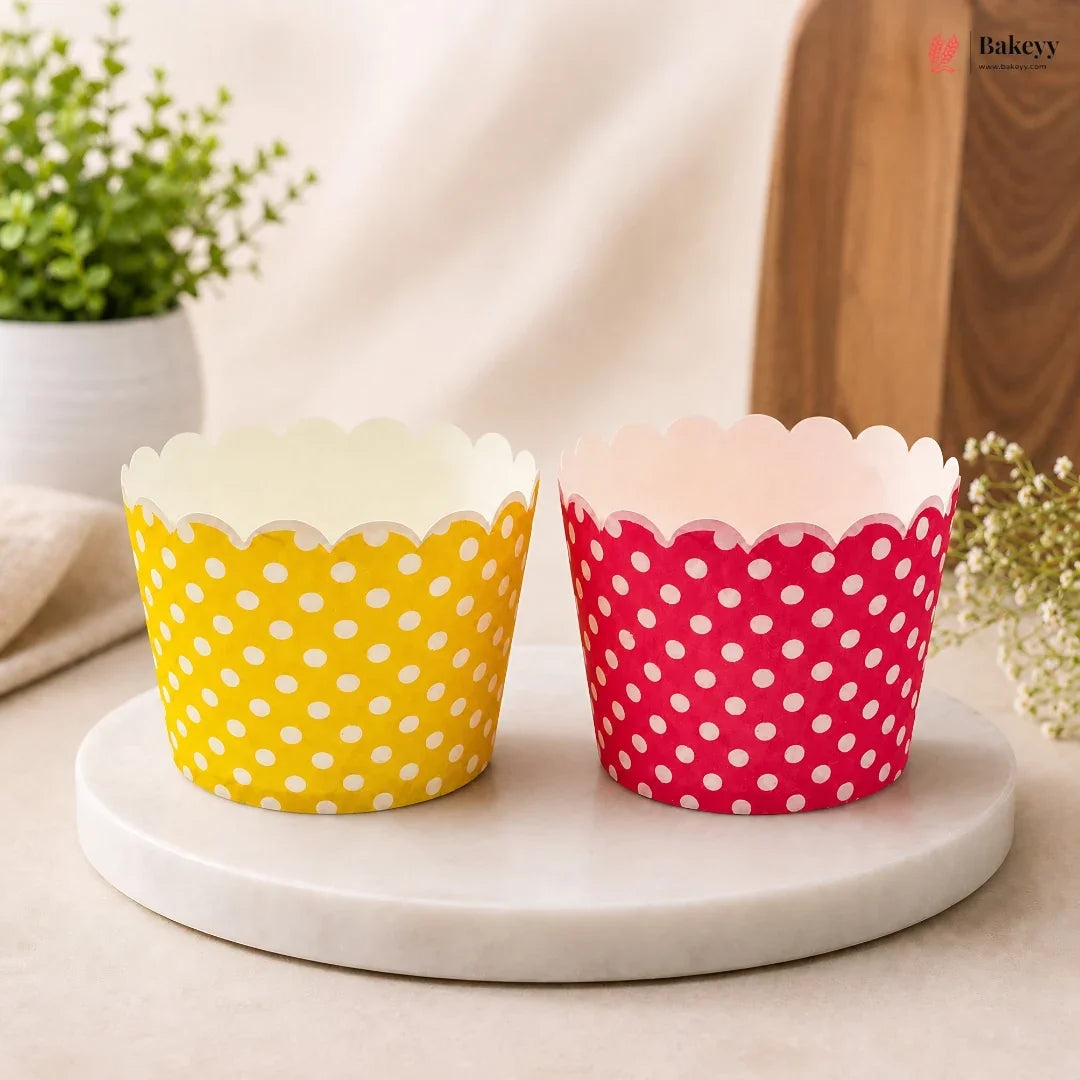 Two polka dot cupcake liners, one yellow and one pink, on a marble surface with a neutral background.