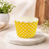Yellow cupcake liner with white polka dots on a marble surface.