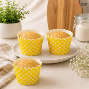 Three cupcakes in yellow polka dot wrappers on a white plate with a neutral background.