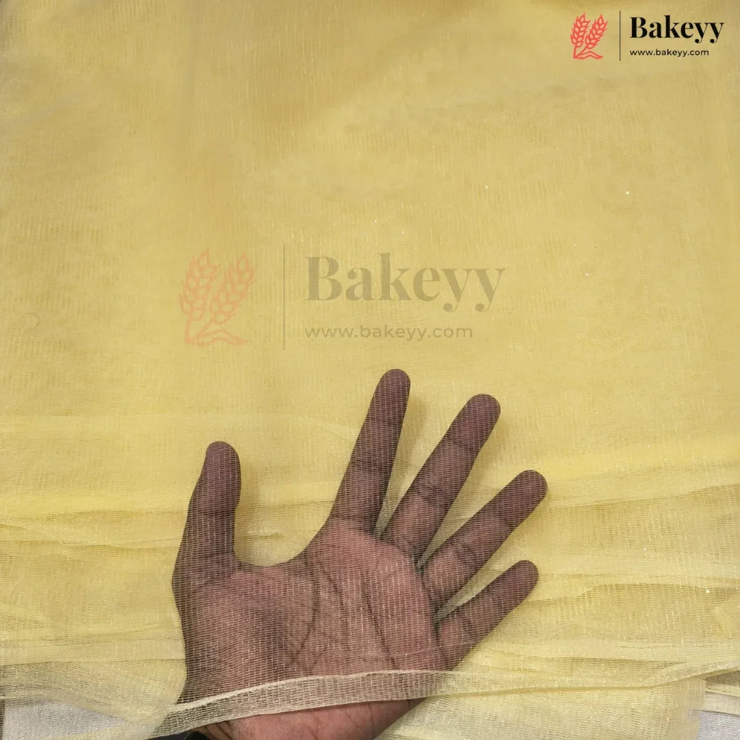 A hand is placed underneath a sheet of pale yellow chiffon fabric to show its texture and transparency. The Bakeyy brand logo is visible in the top right corner.