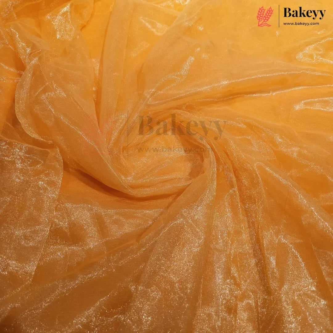 A close-up of sheer, shimmering orange tulle or organza fabric, swirled and draped to show its texture and reflective quality. The Bakeyy brand logo is visible in the top right corner.