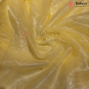 Yellow sheer mesh fabric with a subtle metallic sheen, swirled and draped to show its texture and transparency. A Bakeyy brand logo is visible in the top right corner.