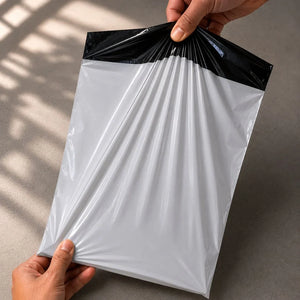 White plastic bag with black top held by a hand on a neutral background