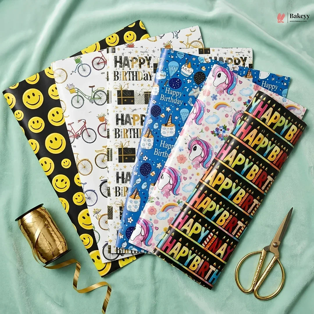 Collection of colorful birthday-themed gift wrap sheets with a spool of ribbon and scissors on a light green fabric background.