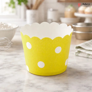 Yellow cupcake liner with white polka dots on a marble surface, branded 'Bakeyy'.