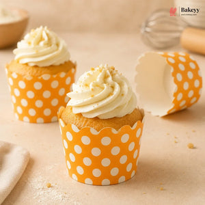 Two cupcakes with white frosting in orange polka dot wrappers on a beige surface, with 'Bakey' branding.