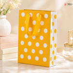 Yellow gift bag with white polka dots on a light wooden surface