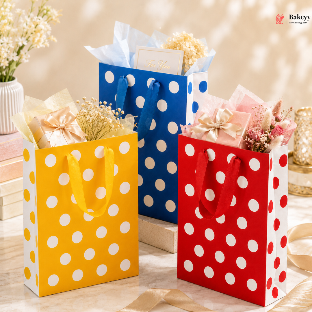 Three polka dot gift bags in yellow, blue, and red with flowers and cards on a blurred background.