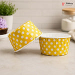 Yellow polka dot baking cups with a lid on a light surface, branded 'Bakeyy'.