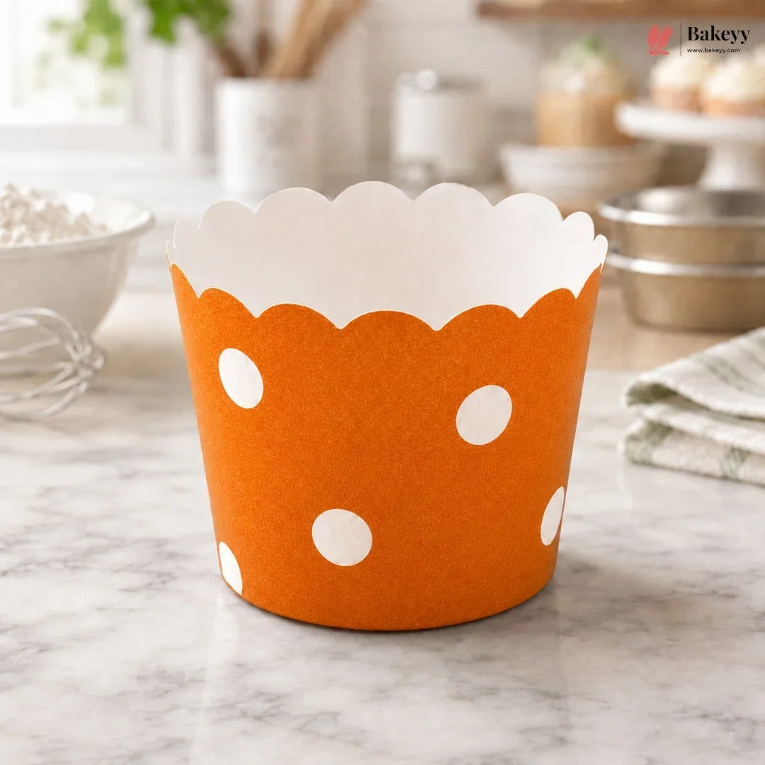 Orange cupcake liner with white polka dots on a marble surface, branded 'Bakeyy'.