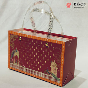 A decorative rectangular bakery gift box with clear plastic handles, featuring a deep red front panel with gold motifs, an orange border, and peacock illustrations, photographed on a light neutral background.