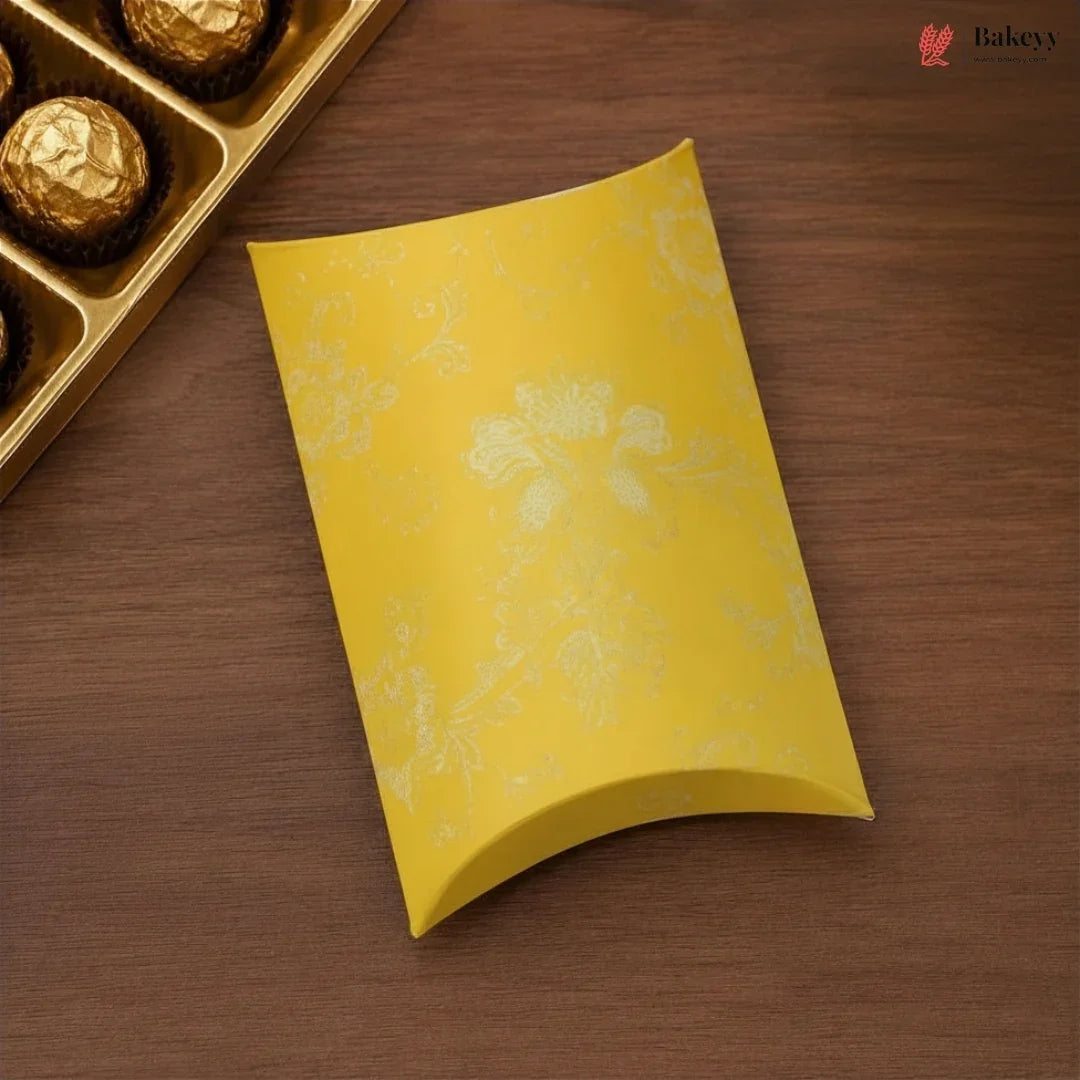 Yellow decorative box on a wooden surface with a gold tray of chocolates.
