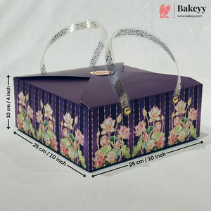 A rectangular purple bakery gift box with floral print on the sides, featuring two clear handles with silver glitter trim and gold-tone clasps. Black dimension lines and text indicate measurements of 25 cm x 25 cm x 10 cm.