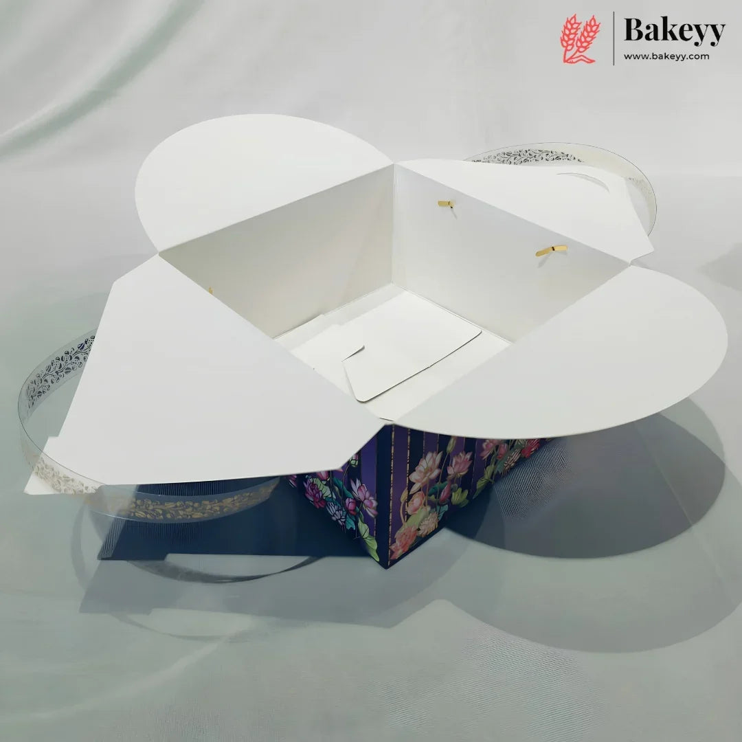 A white bakery gift box with flared lid wings, shown open and empty on a light gray fabric background. A smaller floral-patterned box is partially visible underneath, and a Bakeey logo watermark appears in the top right corner.