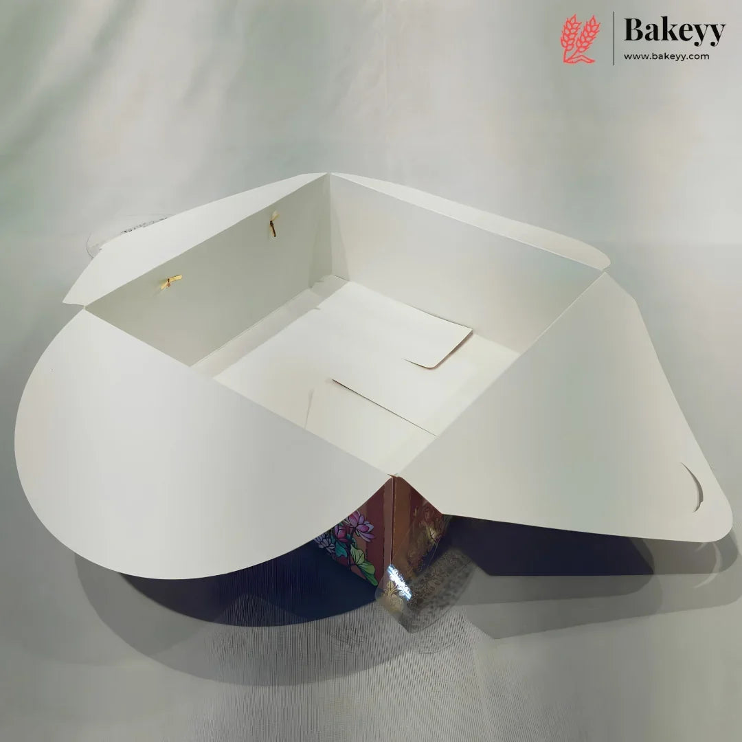 A white cardboard bakery box with flared sides and a triangular base, shown open on a light gray fabric background. The Bakeyy logo is visible in the top right corner.