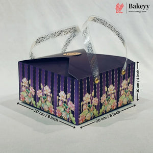 A rectangular bakery gift box with a dark purple lid and floral-patterned sides, shown on a light fabric background with dimension arrows and text indicating 20 cm by 20 cm and 10 cm height. A Bakeyy logo appears in the top right corner.