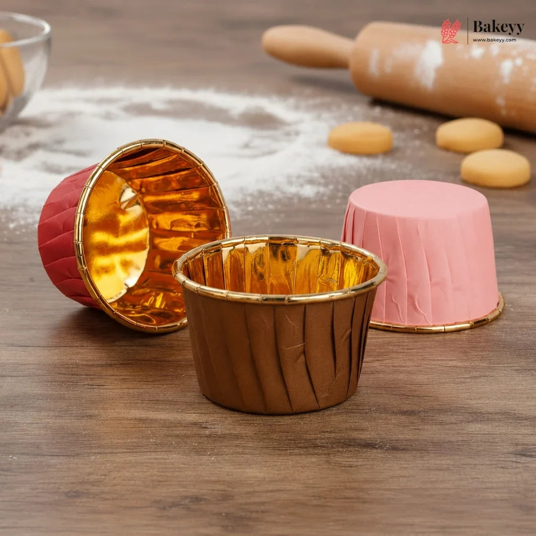 Gold and pink cupcake liners on a wooden surface with baking tools in the background.