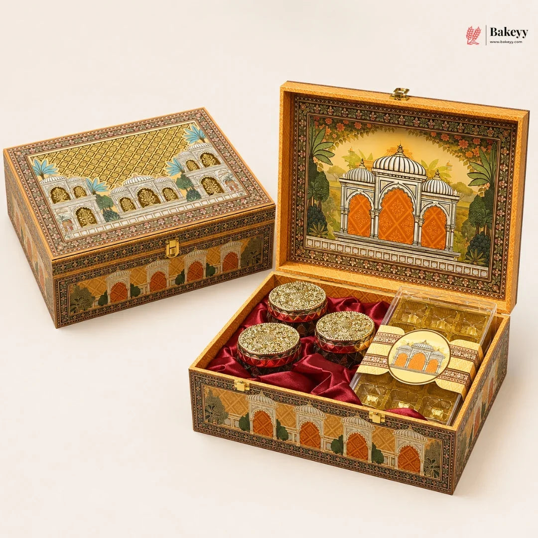 An ornate decorative gift box for sweets, shown closed and open on a light beige background. The box features intricate hand-painted architectural designs in gold, orange, and green, lined with red velvet inside.