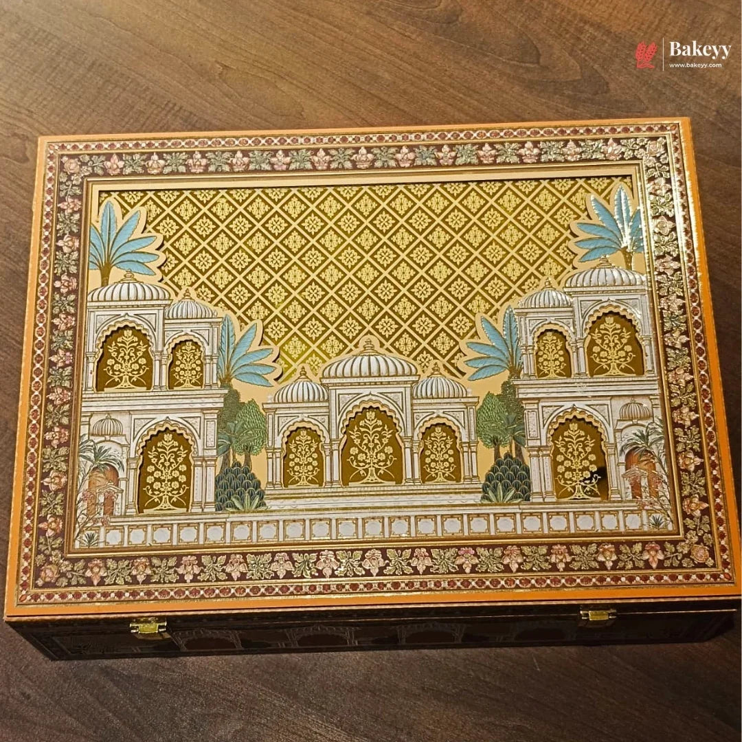 An ornate rectangular decorative box with a hand-painted Indian palace motif on the lid, featuring intricate gold, beige, and blue details, placed on a dark wooden surface.