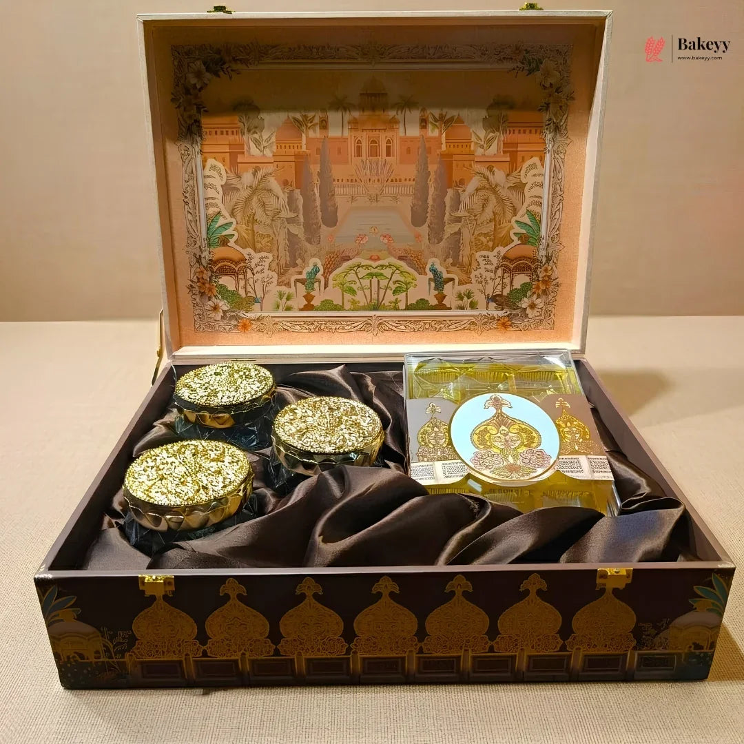 An ornate open gift box containing three small round decorative jars with gold lids and a packaged item, set on a beige surface. The box has a dark brown exterior with gold architectural detailing, and the interior lid features a colorful illustrated scene.