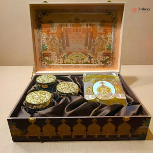 An ornate open gift box containing three small round decorative jars with gold lids and a packaged item, set on a beige surface. The box has a dark brown exterior with gold architectural detailing, and the interior lid features a colorful illustrated scene.