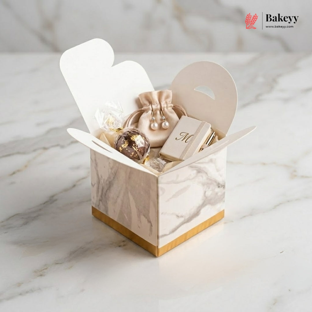 Marble-patterned jewelry box with earrings and a book on a marble surface, featuring the Bakeyy brand.