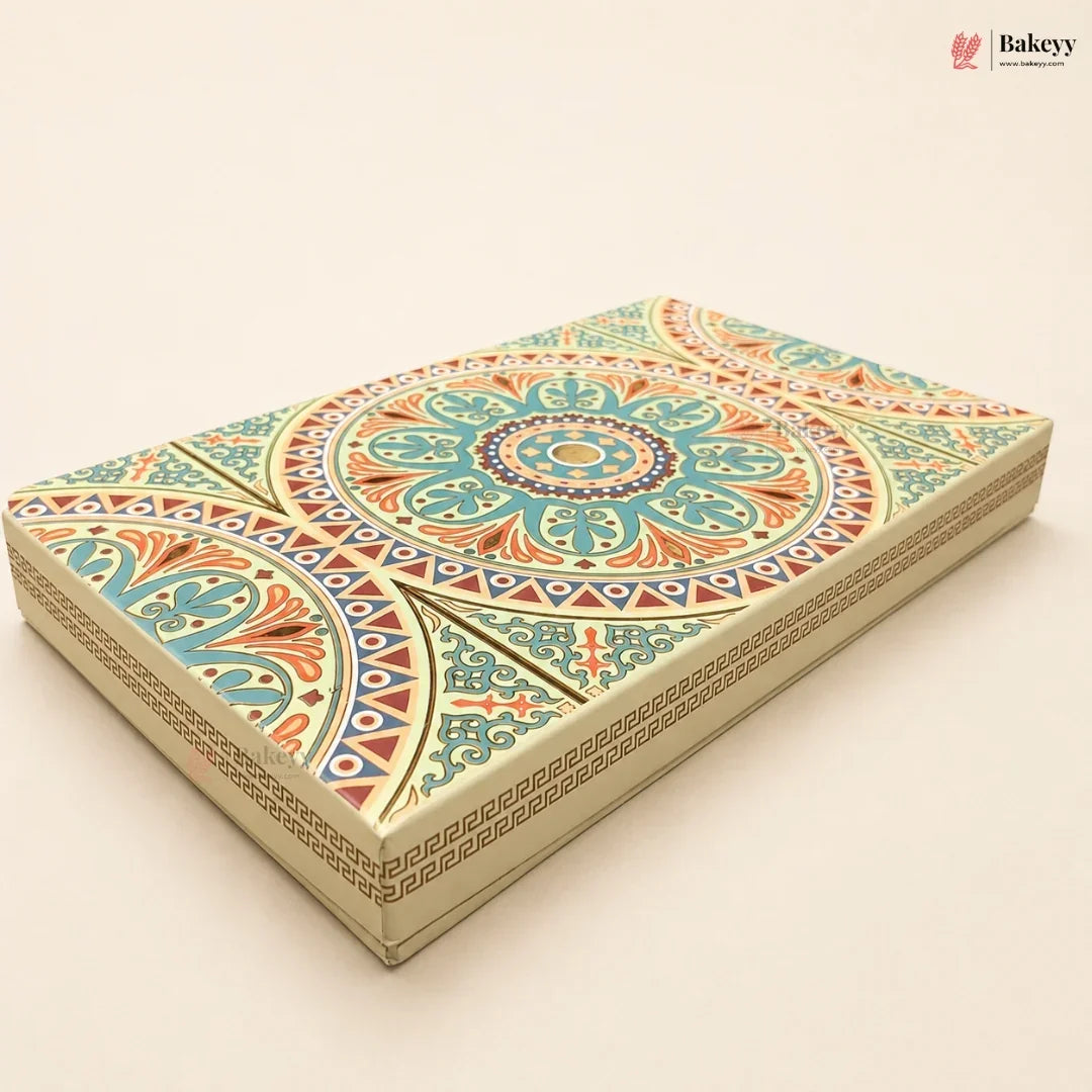 An ornate rectangular cake box with a detailed geometric and floral mandala pattern in teal, orange, red, and cream, shown on a solid light beige background. The Bakeyy logo is visible in the top right corner.
