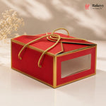 Red gift box with gold accents and a clear window on a beige background, featuring the Bakeyy brand.
