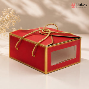 Red gift box with gold accents and a clear window on a beige background, featuring the Bakeyy brand.