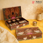 A decorative Bakeyy gift box set displayed on a yellow surface against a beige backdrop. The set includes an open box showing assorted packaged sweets and jars, plus a closed matching box in front.