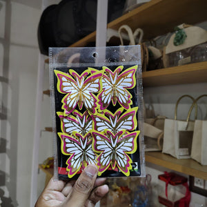Packaged butterfly stickers held in front of a store shelf with bags and products.