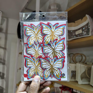 Packaged butterfly decorations held by a hand with a blurred indoor background