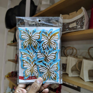 Packaged butterfly-shaped clear stamps held in front of a blurred indoor background