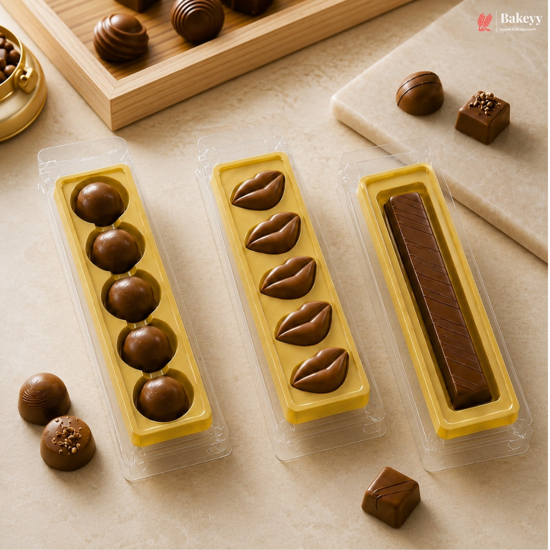 Three yellow chocolate molds in clear plastic packaging, filled with assorted chocolates, arranged on a beige surface with loose chocolates nearby.