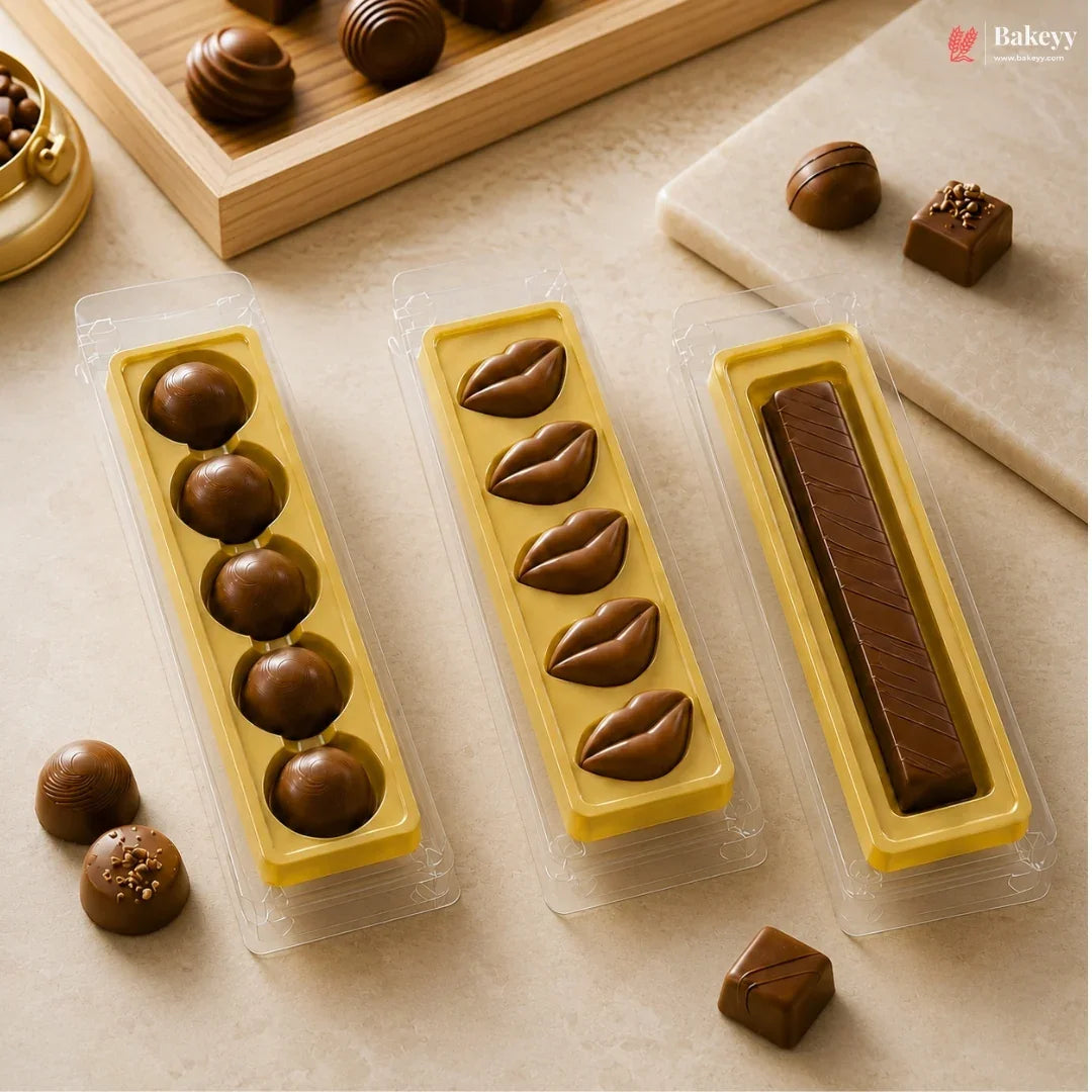 Three yellow chocolate molds in clear plastic packaging, filled with assorted chocolates, arranged on a beige surface with loose chocolates nearby.