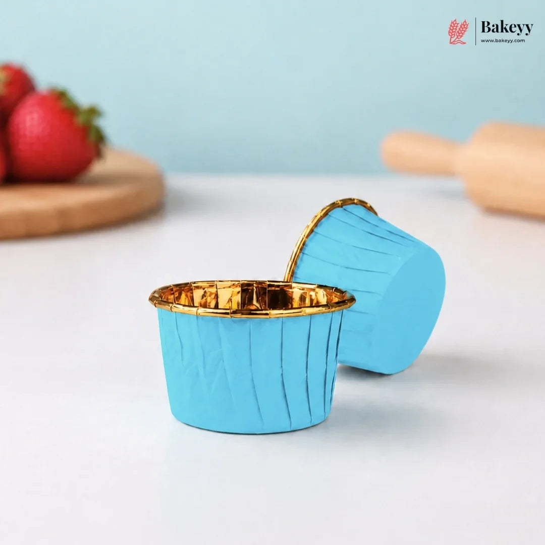 Blue silicone baking cup with gold interior on a white surface, surrounded by strawberries and a rolling pin.