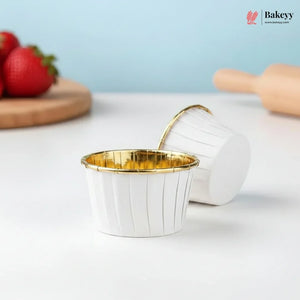 White cupcake liners with gold rims on a light blue background, featuring the Bakey brand.