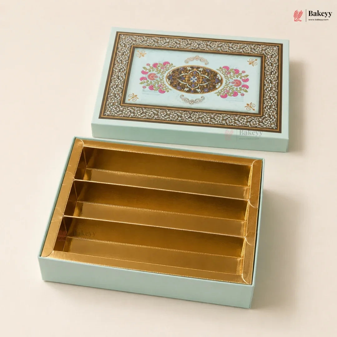 A decorative rectangular gift box set from Bakeyy, featuring a light aqua exterior with an ornate floral and geometric pattern on the lid, and a gold-foil lined interior with four compartments, shown open on a warm beige background.